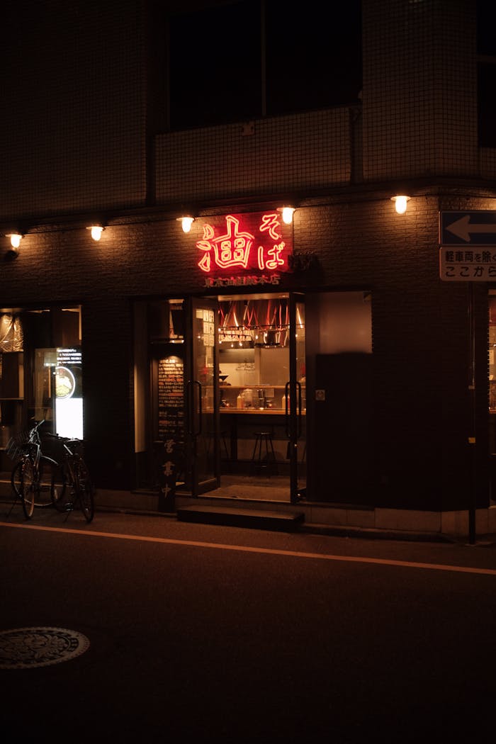 Warmly lit restaurant entrance at night with neon signage, bicycle parked outside.